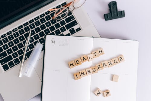 health insurance scrabble tiles on a planner next to a pen that's on a laptop