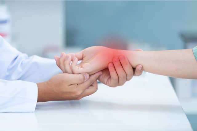 Chiropractor holds patient hand with red area showing where she has wrist pain
